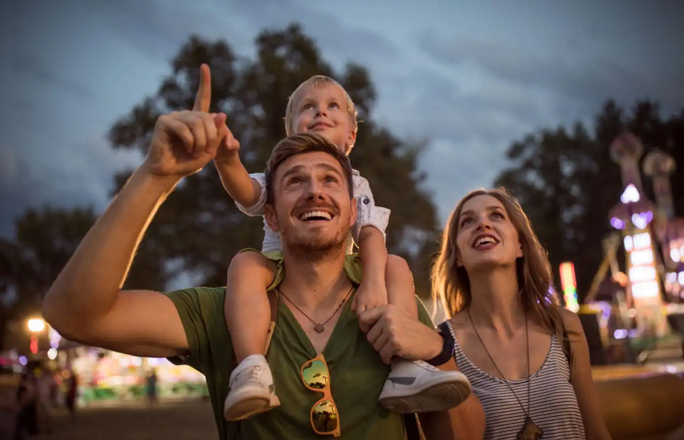 Famille souriante profitant d'une fête foraine en plein air, avec des lumières de manèges en arrière-plan à Gosselies.