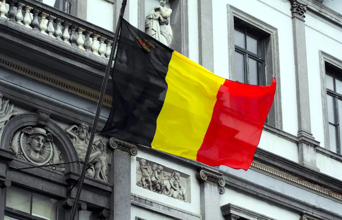 Drapeau belge flottant sur un bâtiment historique avec des sculptures en façade, représentant le patrimoine et l'architecture à Gosselies.